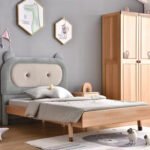 Side angle view of upholstered bear eared toddler bed with beige button tufted center panel and solid wood legs