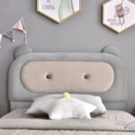 Close-up of grey plush bear ear headboard featuring cream tufted center cushion with two buttons and star pillow