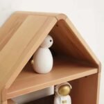 Close-up detail shot focusing on the solid wood grain, sloped roof joinery, and upper shelf depth of the house-frame cabinet with decorative figurines.