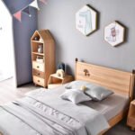 High-angle perspective of a solid wood kids' bed featuring a carved mushroom motif on the headboard, styled with a house-shaped bookshelf and neutral nursery decor.
