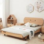 Side perspective of a solid wood bed frame with a carved smiley-face headboard design, low platform profile, and star-shaped accent cushion.