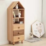 Nursery lifestyle shot of a tall, narrow house-shaped storage tower featuring open display shelving above three stacked pull-out drawers, styled alongside a framed wall print and plush animal decor.