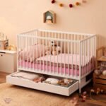 White Amyzel kids wooden crib showcase with the large bottom trundle storage drawer pulled open, revealing organized clothes and blankets underneath the mattress base