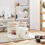 Amyzel round wooden children's activity table and nesting chairs set in a modern nursery room styled with a white wooden leaning ladder bookshelf and toy organizer.