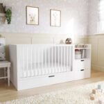 White wooden convertible baby crib with integrated side dresser styled in a bright nursery room decorated with framed animal wall art and a soft plush rug.