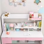 Straight-on eye-level view of a white and pink children's desk surface and upper shelf unit organized with books and decor.