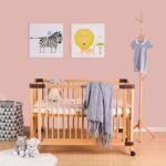 Natural wooden mobile crib decorated with a soft grey fringe throw blanket and stuffed animals in a styled nursery room.