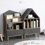 Two pitched-roof house-shaped grey wooden children's book organizers featuring front-facing book display racks and vertical dividers on splayed legs.