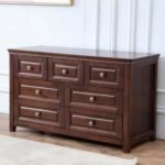 Wide dark wood 7-drawer dresser styled against a white paneled accent wall on a light area rug.