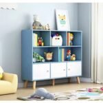 Blue children's toy storage bookshelf unit styled in a modern nursery next to a cozy reader chair and floor play rug.