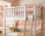 Modern white solid wood bunk bed featuring high top-bunk safety guardrails, a sturdy attached access ladder, and a pink decorative arch wall background.