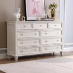 Off-white 9-drawer French country wooden dresser styled with a framed portrait, a flower vase, and classic decor on top.