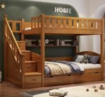 Premium honey oak finish wooden twin-over-twin bunk bed featuring a side storage staircase, a built-in internal bookshelf hutch, and dual under-bed drawers against a dark green wall.
