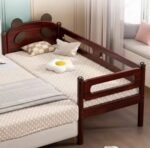 Rich dark mahogany finish wooden toddler bed , Amyzel co-sleeping baby bed with protective guardrails and whimsical bear-eared headboard, cozy kids nursery furniture setup.