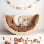 Natural wooden Montessori climbing arch inverted to serve as a cozy rocking lounge chair, outfitted with a thick brown tufted cushion and plush decorative pillows.