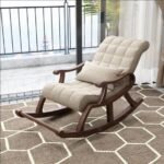 Dark wood rocking armchair upholstered in tufted off white fabric with matching support pillow on white background.