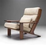 Side perspective of a minimalist mid-century wooden lounge chair with natural beige fabric cushioning.