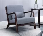 Grey fabric mid-century modern accent armchair with dark walnut wooden frame and lumbar pillow on patterned rug