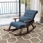 Dark wood rocking armchair upholstered in tufted blue fabric with matching support pillow on white background.