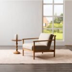 Minimalist cream accent chair styled in modern living room beside carved wooden side table near large window