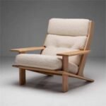Angled view of a solid wood accent armchair with plush cream-beige tufted upholstery and broad wooden armrests.