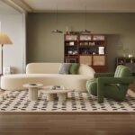 Modern living room interior featuring a beige curved modular sofa and a sage green channel tufted armchair on a geometric patterned rug