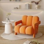 Bright orange plush channel upholstered accent chair with solid block armrests set on a white round carpet