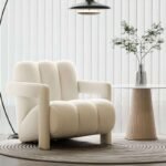 Off-white plush channel tufted armchair on a round ribbed area rug beside a white fluted accent end table