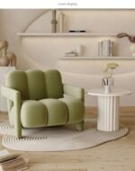 Sage green velvet channel tufted armchair set on an asymmetrical white rug with a white fluted pedestal side table