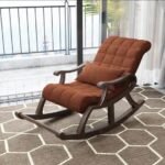 Dark wood rocking armchair upholstered in tufted brown fabric with matching support pillow on white background.