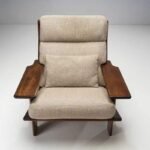 Front view of a low-slung mid-century wooden accent chair upholstered in beige textured fabric with a matching lumbar support pillow.