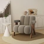 Light grey channel-tufted lounge chair featuring dark wood V-legs placed on a layered round carpet with minimalist decor.