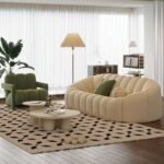 Cream channel tufted curved sofa paired with a sage green plush accent chair on a geometric diamond area rug in a modern living room