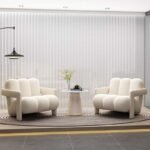Pair of cream white modern padded armchairs facing each other across a small round fluted side table in a minimalist living room setup