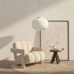 Cream white plush channel back armchair resting on a round woven jute rug next to a dark wood tripod end table