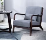 Grey fabric mid-century modern accent armchair with dark walnut wooden frame and lumbar pillow on patterned rug