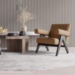 Camel tan leather accent chair with dark walnut V-frame legs and structured armrests set in front of a vertical fluted accent wall.