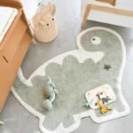Close up view of Amyzel dinosaur shaped children's rug, plush green animal floor mat with plush toddler toys and puzzle blocks in playroom corner.