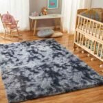 Amyzel mixed grey and white tie dye fluffy shag rug, variegated multi tone plush children's carpet styled next to a natural wood baby crib and rocking chair.