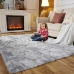 Amyzel light grey fluffy shag area rug for cozy living room layout, thick high pile kids playroom carpet with a young girl reading on the floor by a fireplace.
