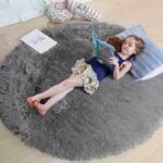 Neutral light grey circular fluffy rug for children's room, modern plush round shag carpet for nursery, soft minimalist kids floor accent mat.