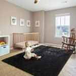 Large black plush shag rug in toddler bedroom, soft rectangular fluffy area carpet, light natural wood baby crib, vintage wooden rocking chair by window.