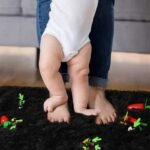 Baby feet standing on ultra soft black shag rug, thick pile fluffy children's playroom carpet, high density plush nursery mat with toy carrots.