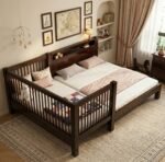 Premium dark-polished wooden baby cot extension seamlessly joined to a matching master bed, featuring a modern slatted safety railing in a contemporary, minimalist bedroom.